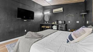 A bedroom with a bed, a TV, a microwave, and a dresser.