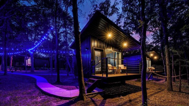 Une cabane dotée d’une terrasse, entourée d’arbres et illuminée par des guirlandes lumineuses.