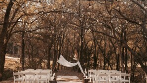 Une cérémonie de mariage organisée dans une forêt, avec des chaises blanches et une arche décorée de voiles blancs.