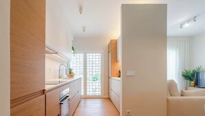 A modern kitchen with wooden cabinets and a central island, leading to a living area with a sofa and a plant. - Stylish & Spacious Apartment by HostWise (Porto)