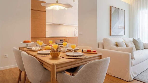 A modern living room with a white sofa, a wooden dining table set with plates and glasses, and a kitchen in the background. - Stylish & Spacious Apartment by HostWise (Porto)
