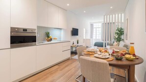 Una cocina moderna con armarios blancos, horno empotrado y comedor con mesa de madera lista para el desayuno.