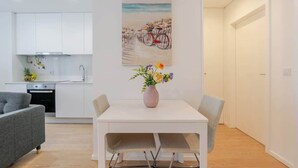 Una cocina moderna con armarios blancos, un comedor con mesa y sillas blancas, y un cuadro de una bicicleta en la pared.
