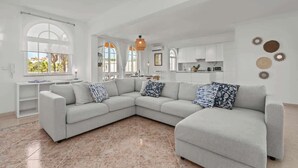 Een ruime woonkamer met een grote hoekbank, een witte console tafel en een keuken op de achtergrond.