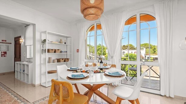 Een eetruimte met een ronde tafel, witte stoelen en een buffetkast met etenswaren.