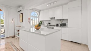 Een moderne keuken met witte kasten, een centraal eiland en een groot raam dat voor natuurlijk licht zorgt.