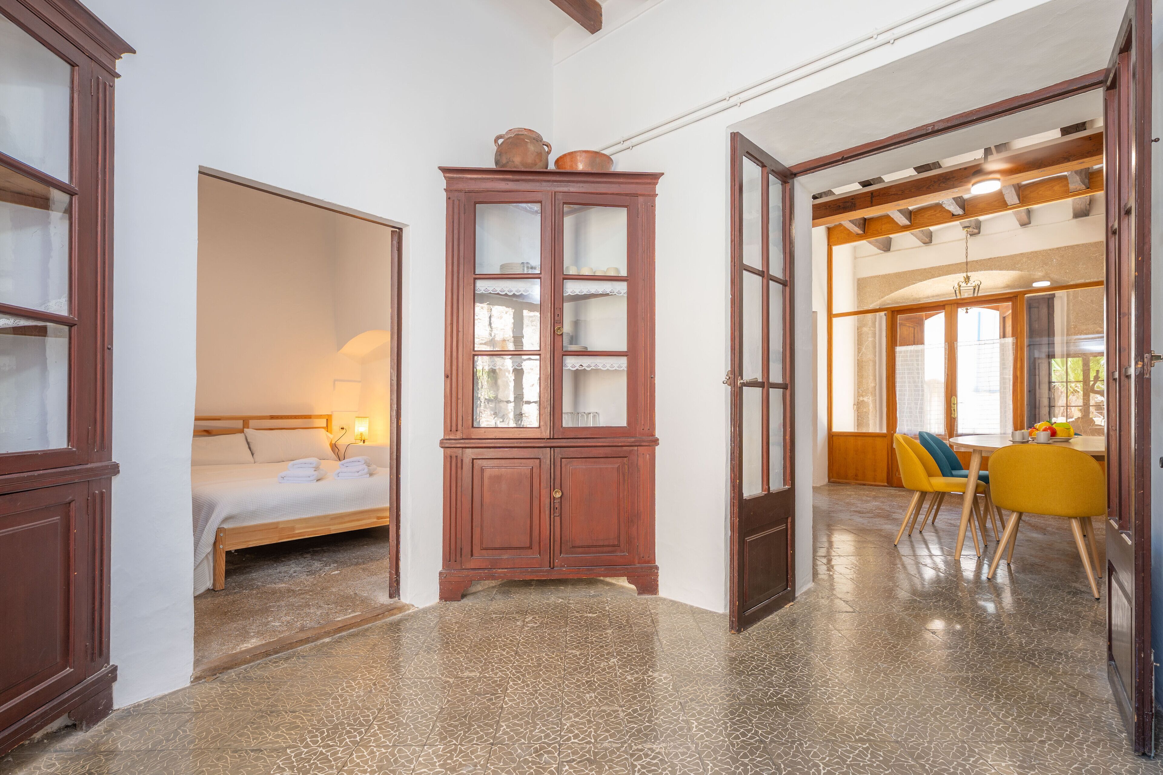 A hotel room with a bed, a wooden cabinet, and a dining area with yellow chairs.