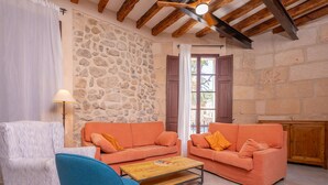 A cozy living room with stone walls, wooden beams, a white armchair, two orange sofas, a blue chair, and a wooden coffee table. - CASA MALLORQUINA CON ENCANTO - Rustic village house with private pool and free WiFi (Mancor de la Vall)