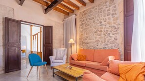 A living room with a stone wall, wooden beams, a blue chair, a white armchair, an orange sofa, and a wooden coffee table. - CASA MALLORQUINA CON ENCANTO - Rustic village house with private pool and free WiFi (Mancor de la Vall)