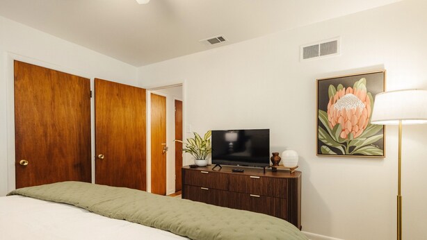Un dormitorio con cama, televisión, cómoda y un cuadro en la pared.