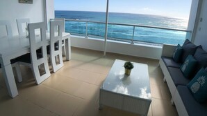 Un balcon avec vue sur l’océan, un ensemble de mobilier de salle à manger blanc et un canapé avec des coussins.