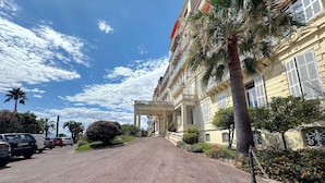 A building with a grand entrance, parked cars, and palm trees. - Studio l`Atelier – Parking & Beaches 15 min Walk (Cannes)