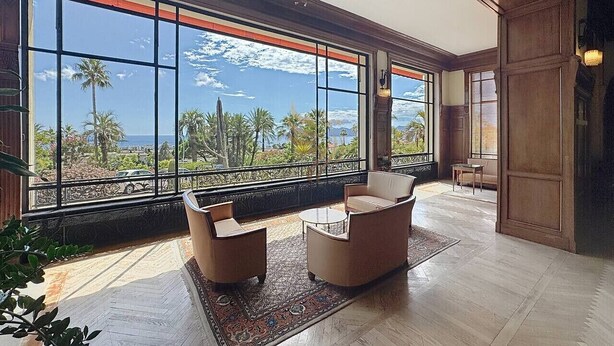 A spacious room with large windows offering a view of palm trees and the sea. There are two sofas and a small table. - Studio l`Atelier – Parking & Beaches 15 min Walk (Cannes)