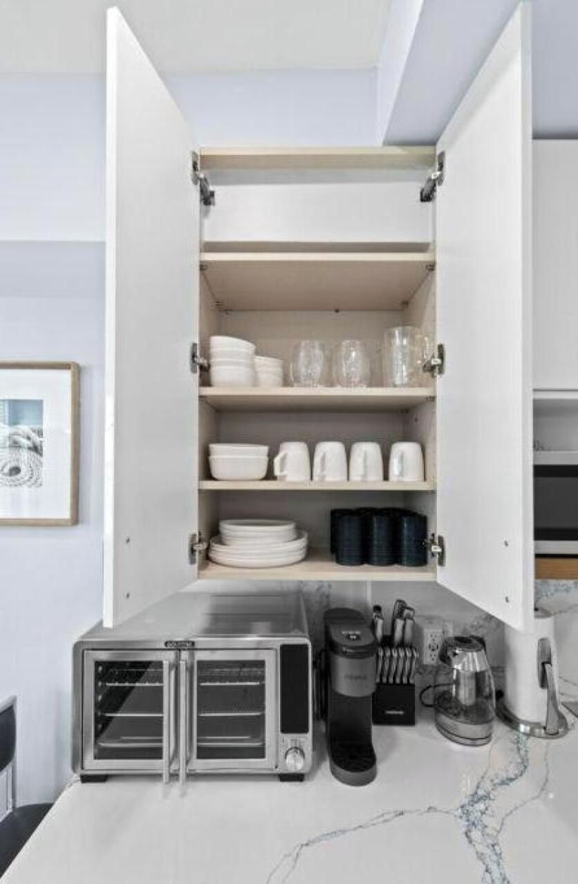 A kitchen with open cabinets displaying dishes, glasses, and cookware. There are two coffee makers and a toaster oven on the counter.