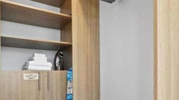 Une chambre d’hôtel avec une armoire en bois, un lit avec un oreiller à rayures et une valise posée sur le sol.