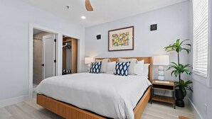 Une chambre moderne avec un lit en bois, des tables de chevet, une petite table de nuit, une plante en pot et une porte donnant sur un placard.
