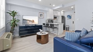 Un salon moderne avec un téléviseur à écran plat, un canapé bleu, une table basse en bois et une plante en pot.