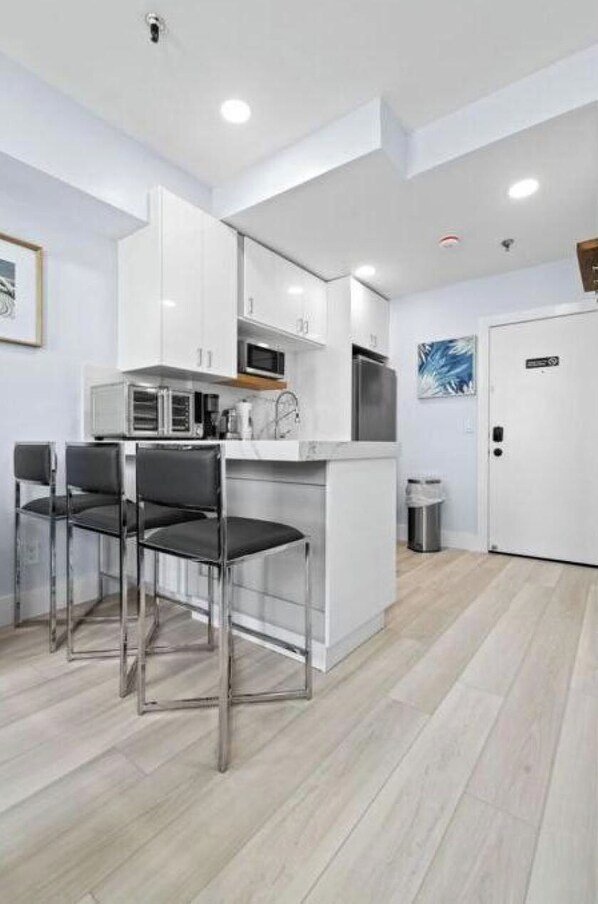 A modern kitchen with white cabinetry, a central island, and bar stools. - REnov/StepsTOBeach/Pool/Shore 1br (Palm Beach)