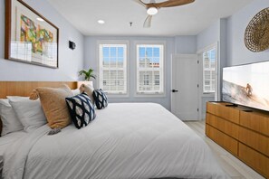 A bedroom with a bed, a television, a ceiling fan, and two windows with blinds. - REnov/StepsTOBeach/Pool/Shore 1br (Palm Beach)