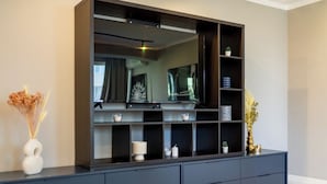 A modern living room with a large flat-screen TV mounted on a dark wooden entertainment unit. There are multiple shelves with decorative items and a few small potted plants. - Golden Glow Hideaway (Bucharest)
