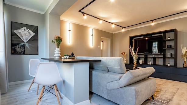 A modern living room with a grey sofa, a white chair, a small bar area, and a TV mounted on the wall. - Golden Glow Hideaway (Bucharest)