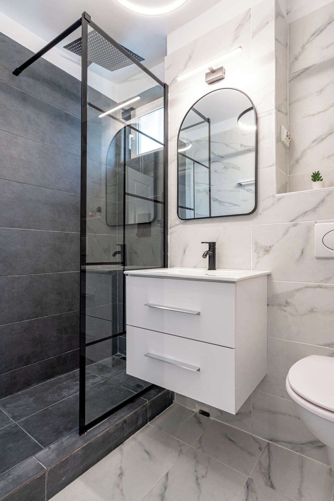 A modern bathroom with a glass shower enclosure, a white vanity with a marble countertop, and a large mirror above the sink.