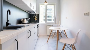 A modern kitchen with white cabinets, a black faucet, and a round table with chairs. - Golden Glow Hideaway (Bucharest)