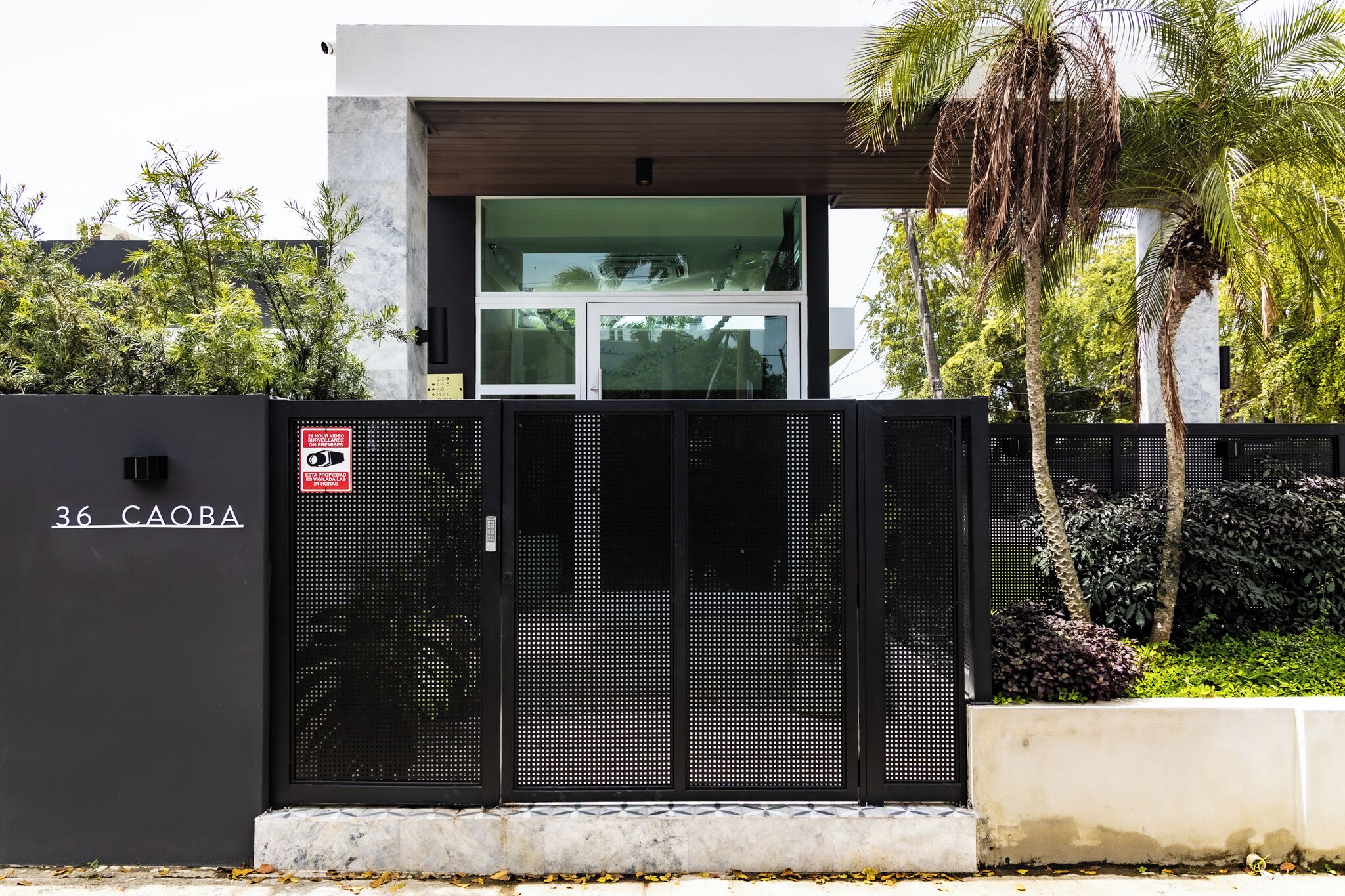 A modern building with a black metal gate, a sign reading "36 CAOBA", and a glass door.
