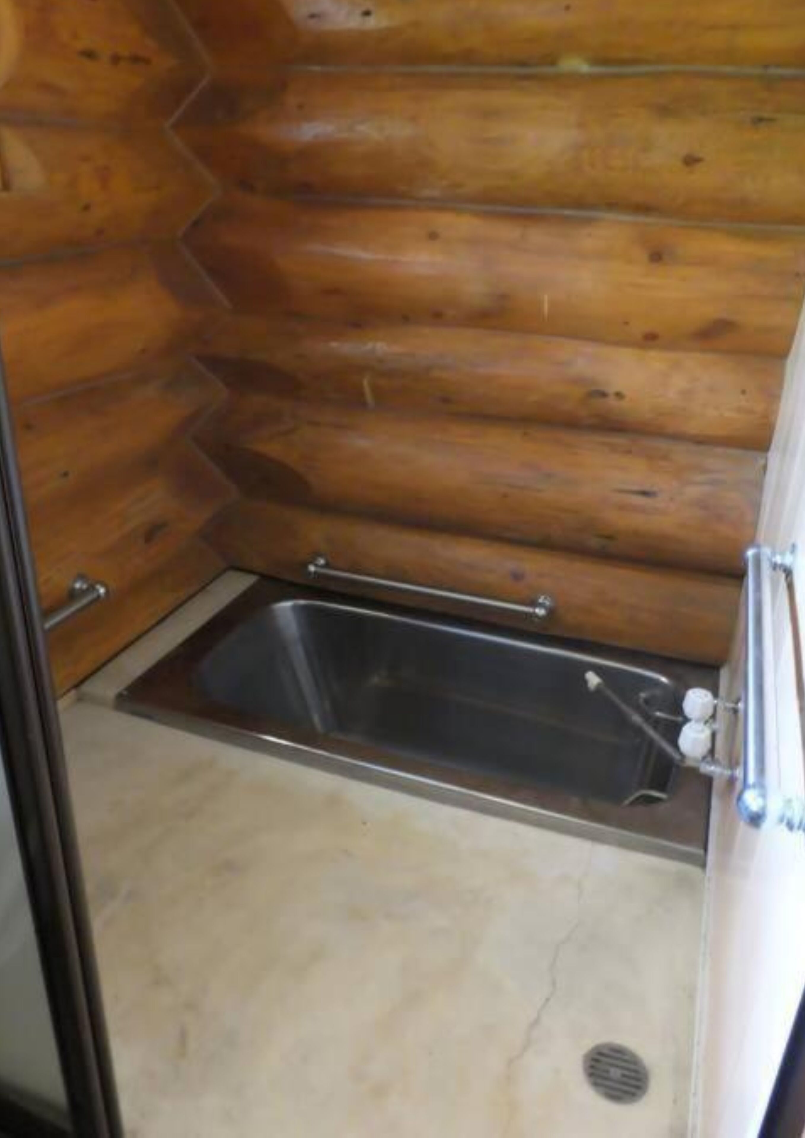 A wooden cabin interior with a metal sink and a small window.