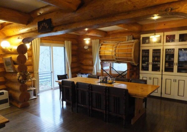 L’intérieur d’un chalet rustique en rondins de bois comprend une grande table à manger en bois placée au centre, des tabourets de bar et un coin cuisine avec des placards.
