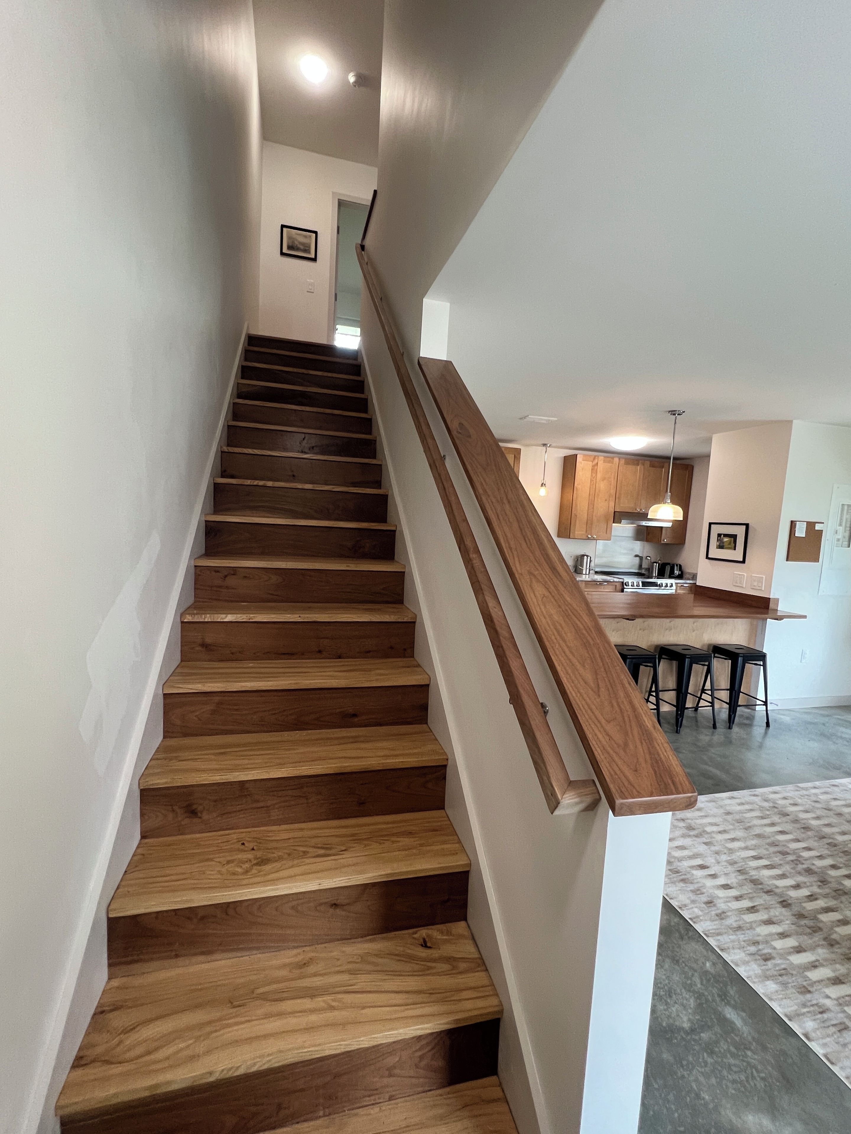 A staircase with wooden steps and a wooden handrail leading to a kitchen area with wooden cabinets and a bar counter.