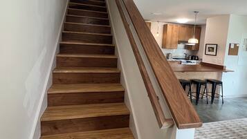 A staircase with wooden steps and a wooden handrail leading to a kitchen area with wooden cabinets and a bar counter.
