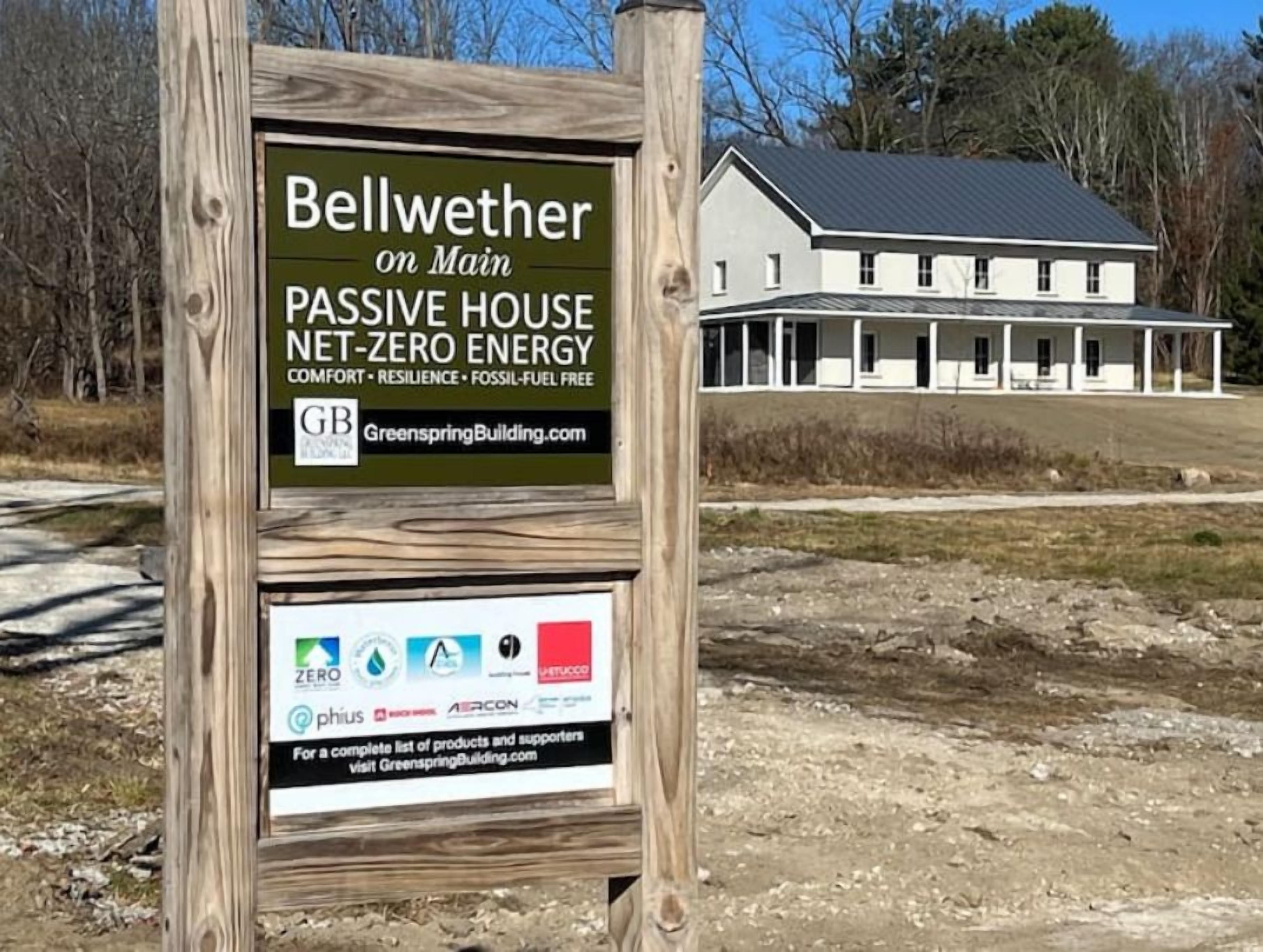 A signboard for a passive house named Bellwether on Main, highlighting its net-zero energy status and listing supporting companies like Greenspring Building, ZERO, PHIUS, and AERCON.