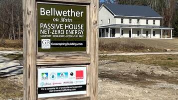 A signboard for a passive house named Bellwether on Main, highlighting its net-zero energy status and listing supporting companies like Greenspring Building, ZERO, PHIUS, and AERCON.