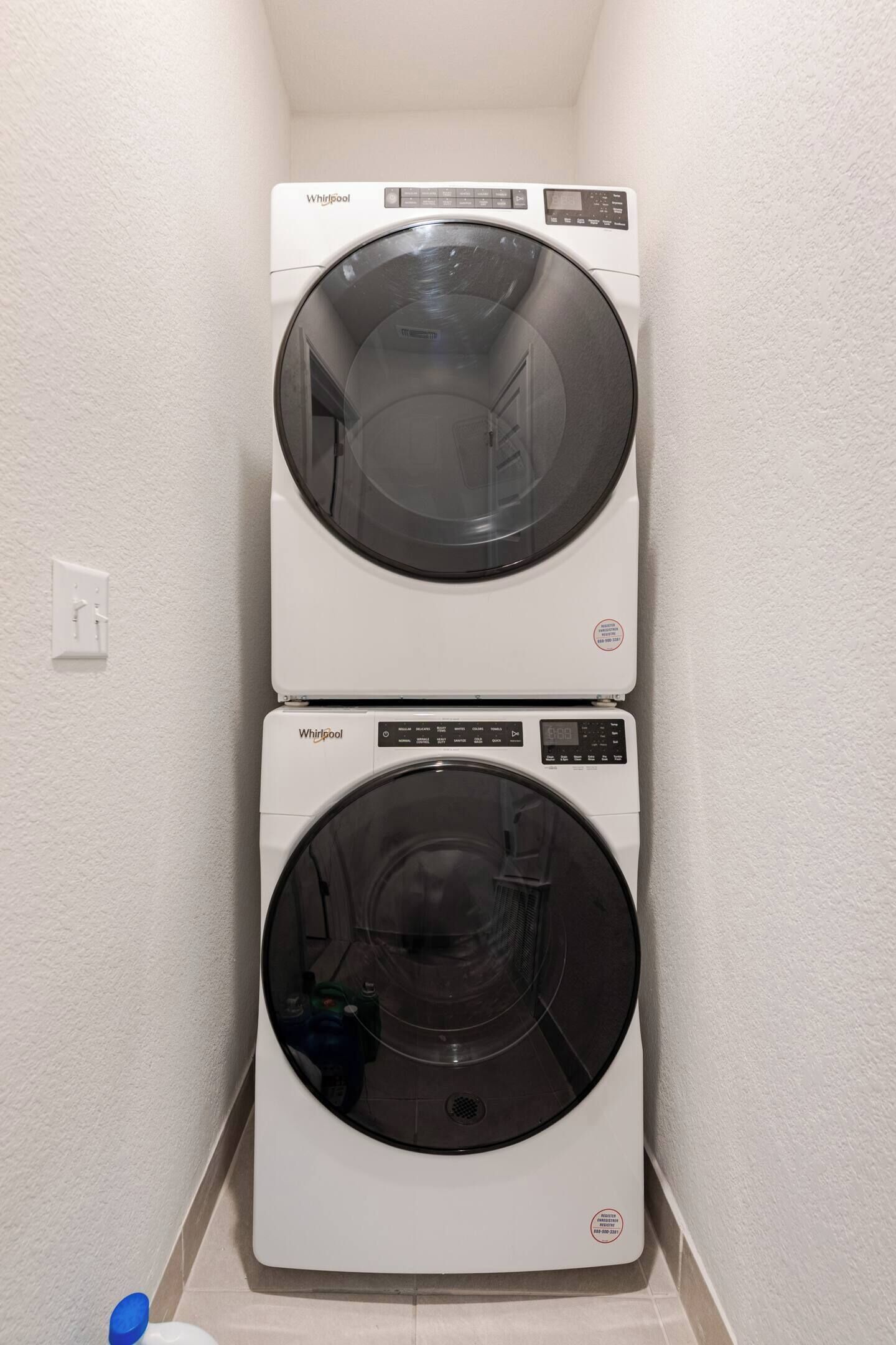 Two stacked Whirlpool washing machines in a corner with a white wall and tiled floor.