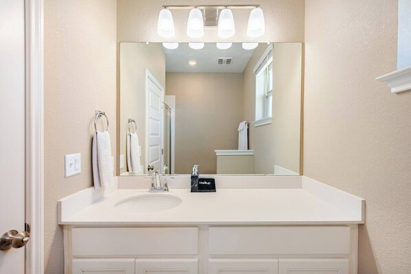 A bathroom with a white vanity, a large mirror, and a light fixture above the mirror. - Luxury 2S Condo Hot Tub Gym Pool Airport (Austin)