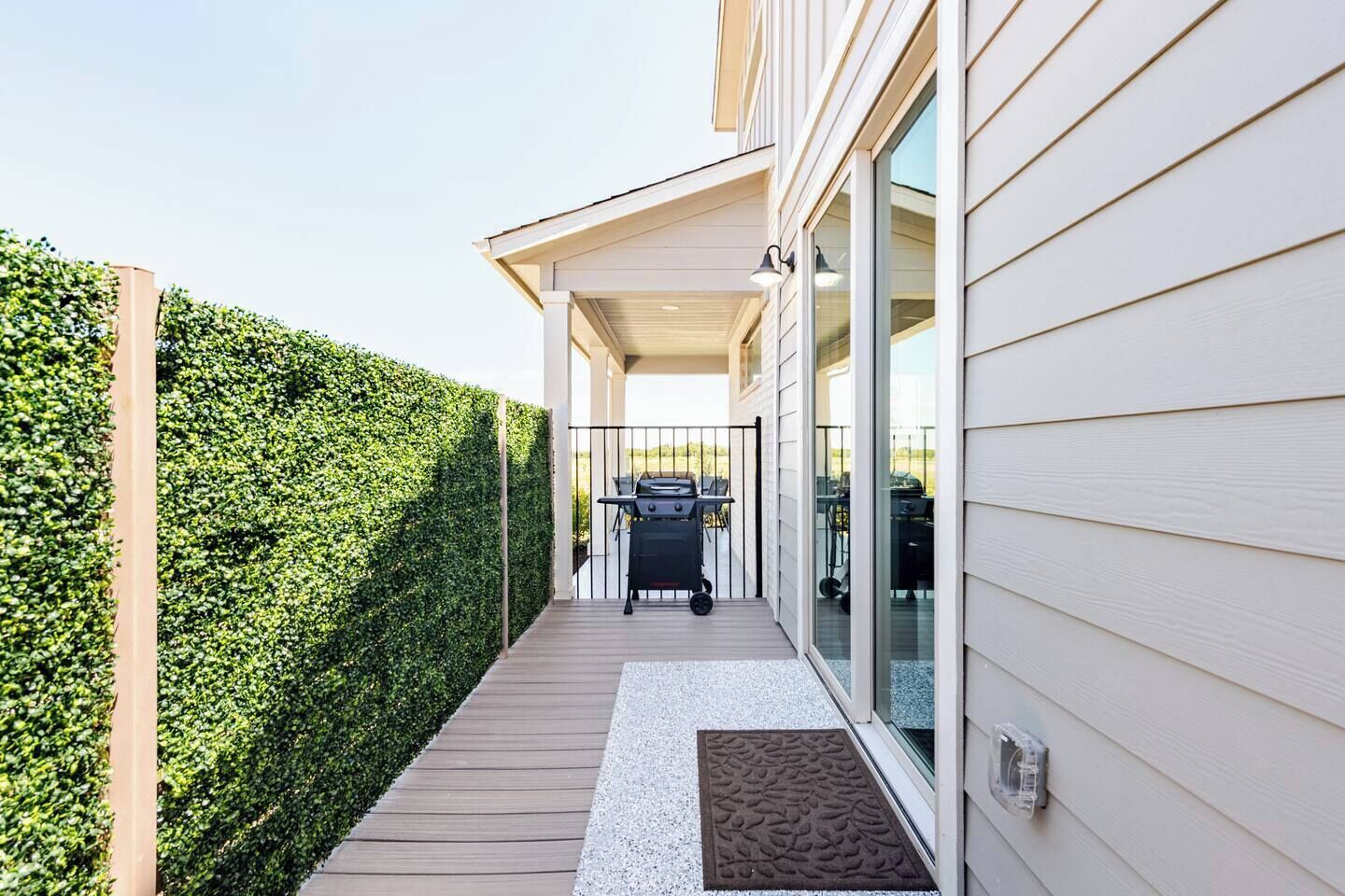 A covered outdoor area with a grill, a wooden deck, and a hedge.