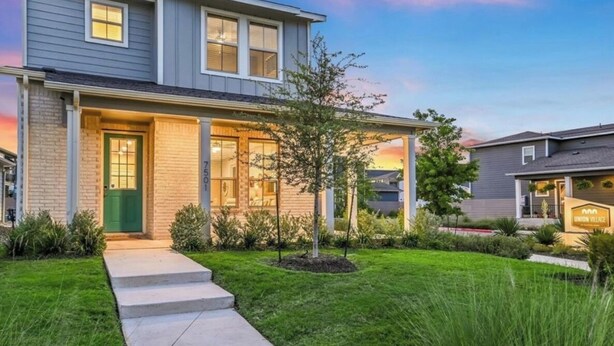 Una casa a due piani con un portico, un prato curato e cielo sereno.