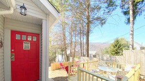 Una puerta roja con un letrero que dice 'Lake Rules', una terraza de madera con mobiliario exterior y vistas a árboles y colinas.