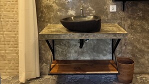 Un baño con un lavamanos de piedra, un espejo, una cortina de ducha y piso de azulejos.