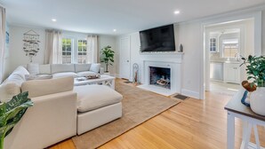 Una sala de estar moderna con chimenea, un televisor grande y una cocina visible a través de un vano abierto.