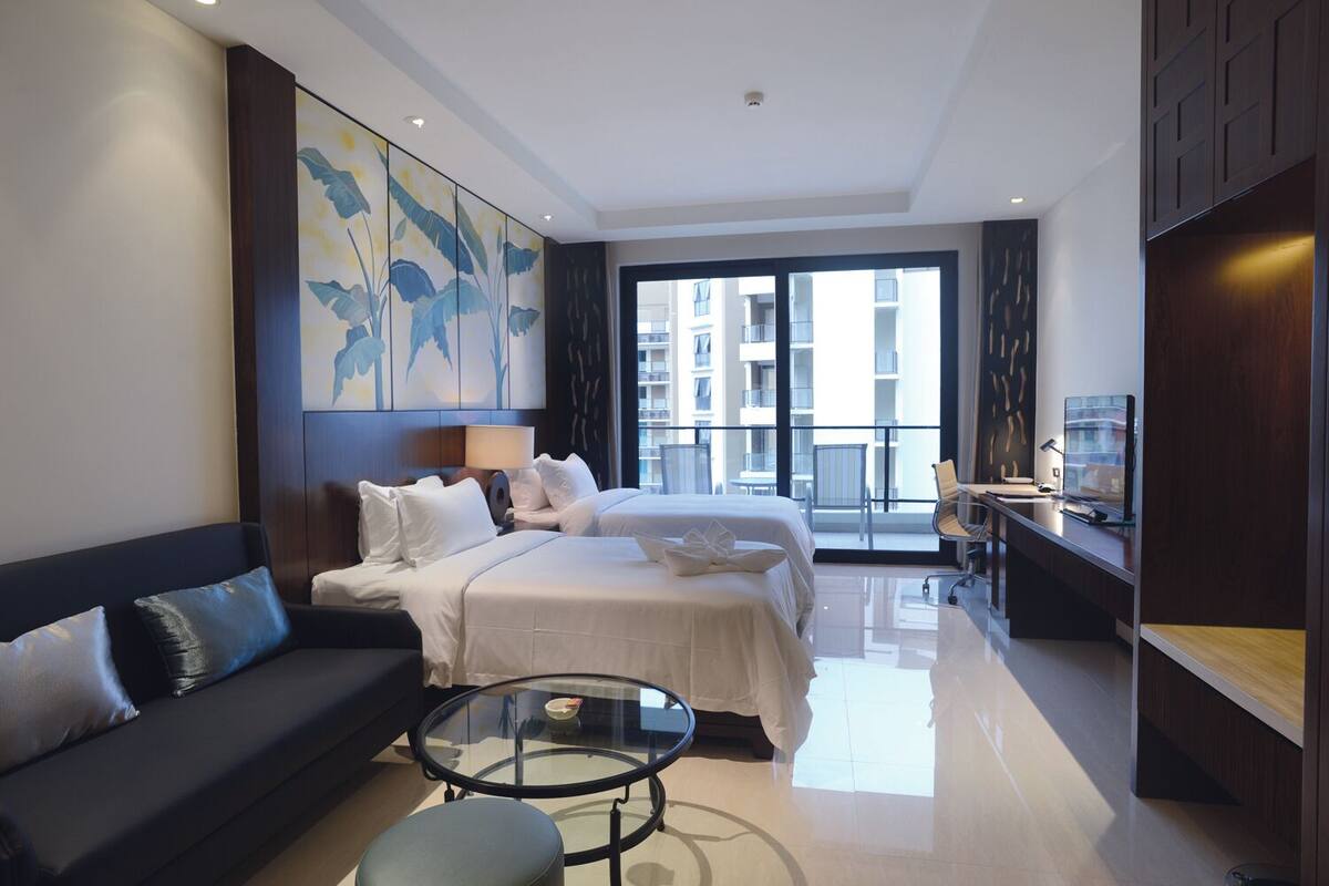 Una habitación de hotel moderna con una cama grande, un sofá, una mesa de centro de vidrio y un escritorio con una silla.