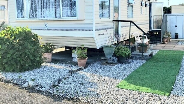 A mobile home with a covered porch, potted plants, and a gravel driveway. - Comfort & Peace 5Berth Family Friendly Park (St Austell)