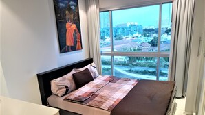 Un dormitorio con un ventanal grande, una cama con ropa de cama estampada y un cuadro en la pared.