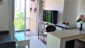 Una sala moderna con sofá, televisor, mesa de comedor y balcón con vista a follaje.