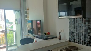 Una cocina moderna con encimera blanca, armarios negros y salpicadero de azulejos. Hay una zona de comedor con una silla y una mesa.