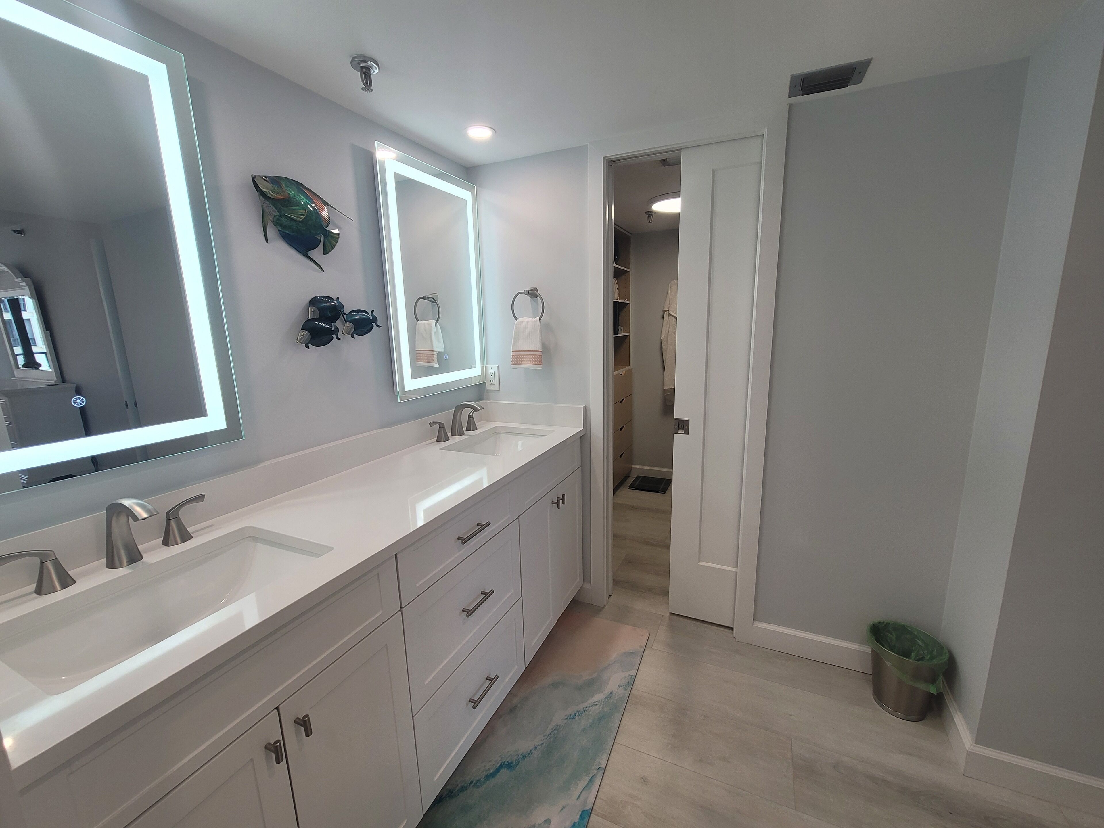 A modern bathroom with two sinks, a large mirror, and a walk-in closet.