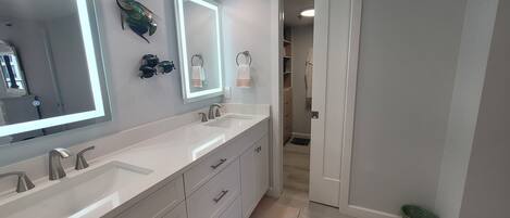 A modern bathroom with two sinks, a large mirror, and a walk-in closet.