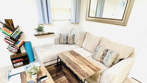 A living room with a sectional sofa, a coffee table with storage, a bookshelf, and a large mirror. - Lake Murray 3BR Retreat with AC and Skylight (La Mesa)
