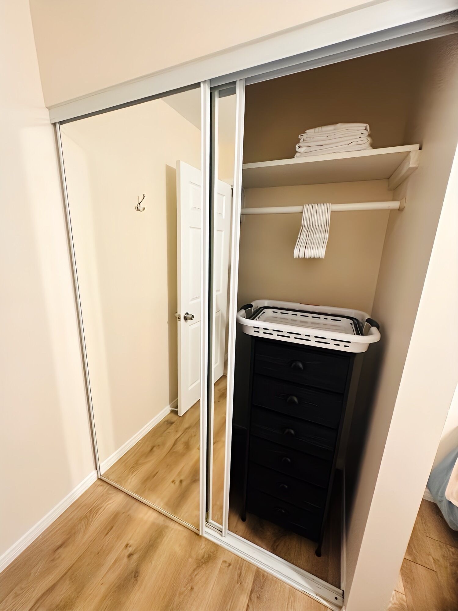 A walk-in closet with a sliding door, a black storage unit, and a white laundry basket on a shelf.